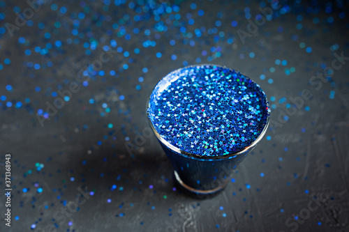 blue shiny stars in a glass on a dark shiny table, top view, holiday cocktail
