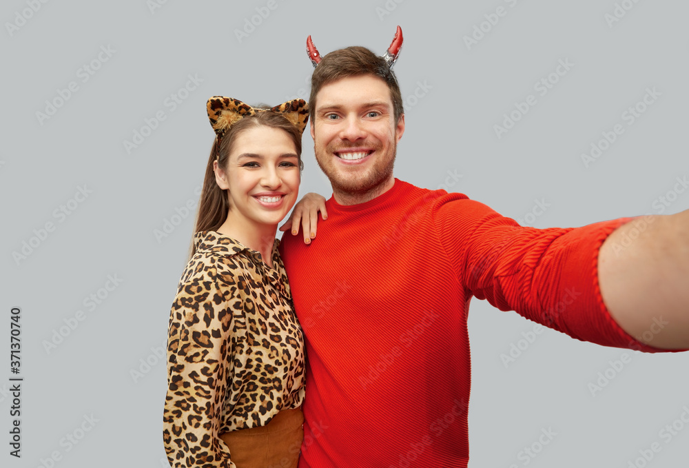 Φωτογραφία holiday and people concept - happy smiling couple in halloween costumes of devil