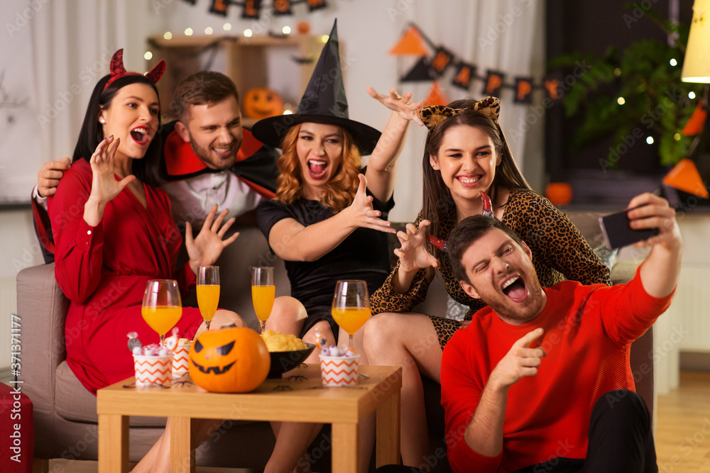 friendship, holiday and people concept - group of happy smiling friends in halloween costumes of vampire, devil, witch and cheetah taking selfie by smartphone at home party at night friendship, holiday and people concept - group of happy smiling friends in halloween costumes of vampire, devil, witch and cheetah taking selfie by smartphone at home party at night