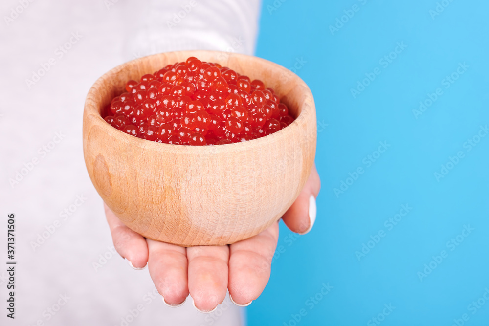 Salmon fish caviar, seafood on wooden jar in hand, isolated on blue background. Salmon fish caviar, seafood on wooden jar in hand, isolated on blue background.