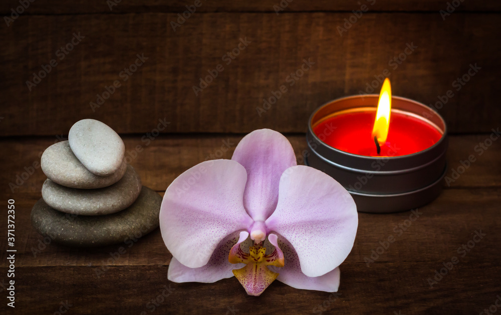 Spa stones with a pink Orchid and a burning candle on a brown wooden background Spa stones with a pink Orchid and a burning candle on a brown wooden background