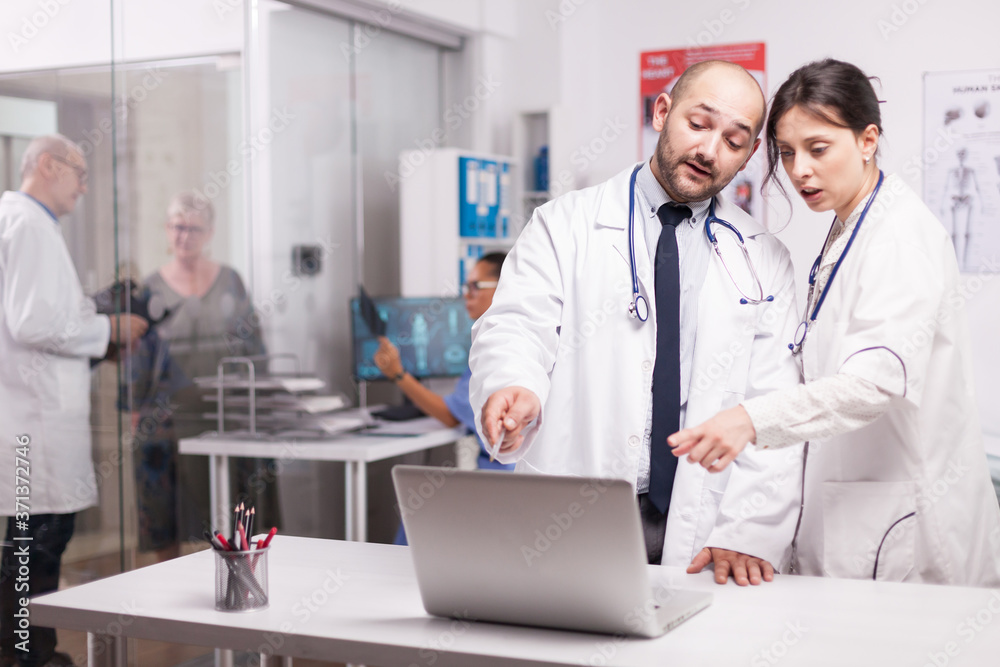 Team of doctor working together in hospital office looking at laptop checking patient report. Senior doctor with old sick man on clinic corridor and nurse is holding x-ray image. Team of doctor working together in hospital office looking at laptop checking patient report. Senior doctor with old sick man on clinic corridor and nurse is holding x-ray image.