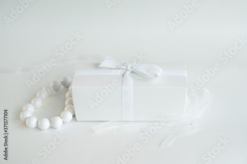 White box tied with a ribbon on a white background. There are beads on the box.