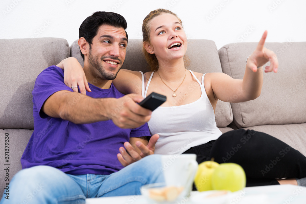 Obraz premium Loving young couple sitting on sofa at home watching TV