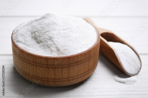 Baking soda in bowl on white wooden table, closeup