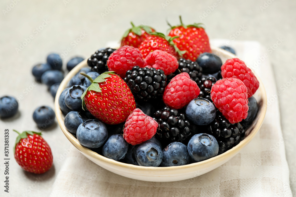 Mix of different fresh berries in bowl on light grey table Mix of different fresh berries in bowl on light grey table