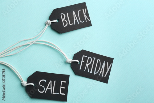Tags with words BLACK FRIDAY SALE on turquoise background, flat lay