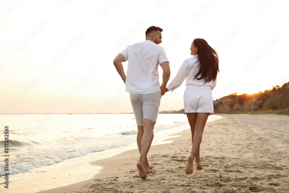 Lovely couple running together on beach at sunset, back view