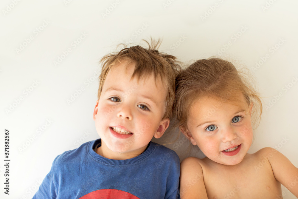 Adorable brother and sister smiling and looking at camera while leaning on white wall Adorable brother and sister smiling and looking at camera while leaning on white wall