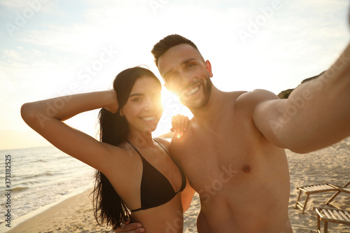 Happy young couple taking selfie on beach at sunset