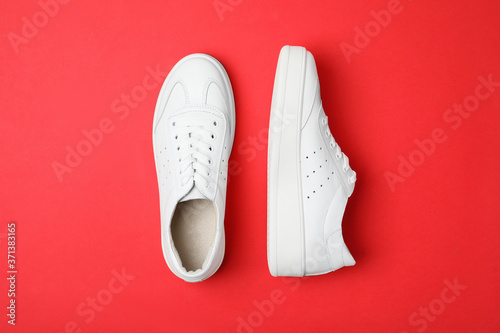 Stylish white shoes on red background, flat lay