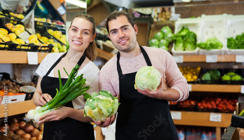 Young smiling man and woman sellers showing green onion and cabbage in supermarket