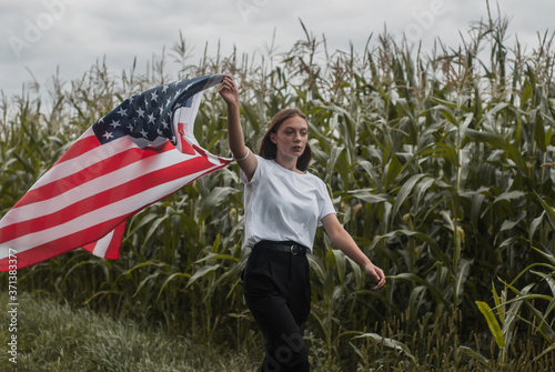 A girl with an American flag walks along a cornfield, labor Day,