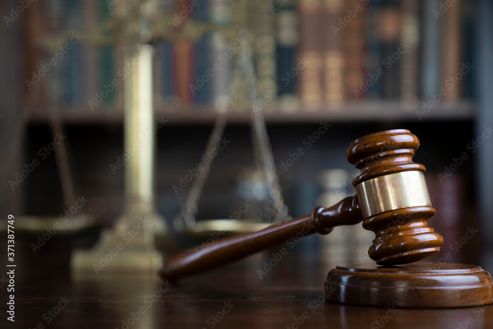 Law theme. Judge chamber. Gavel and scale on brown shining desk. Collection of legal books in the bookshelf.