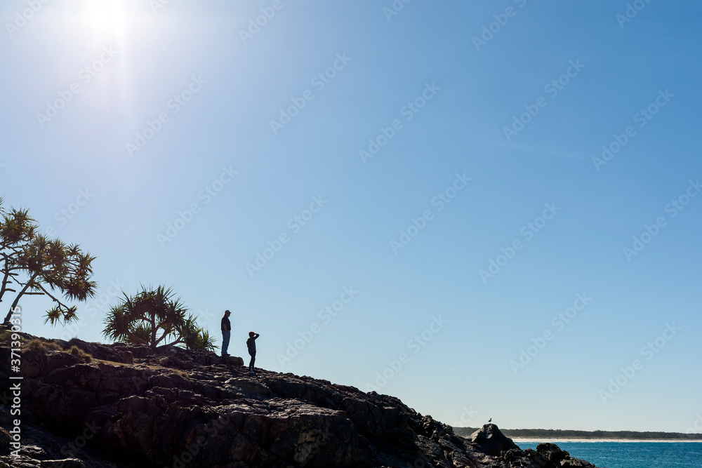 Silhouette of two people standing on the rocky hill near the sea coastline
