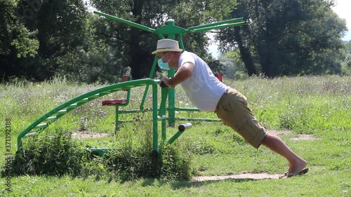 Middle Age Man Wearing Hat and Medical Mask Doing Exercise in Outdoor Gym
