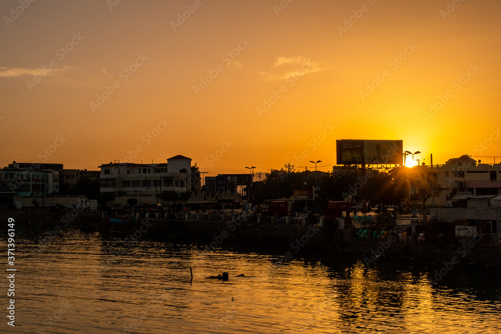 Port Sudan, Sudan. Coast silhouette in a harbor in Port Sudan, with sudanese people trading goods. Old buildings of the city in the background, beautiful orange sunset.