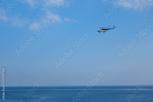 Rescue helicopter is flying above surface of sea. Blue sky is on background