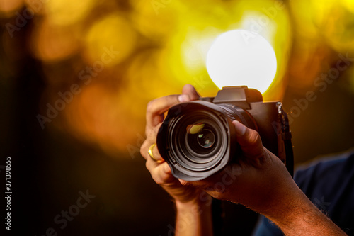 Fotografía Closeup of a black camera holding by Photographer's hand with sunset background