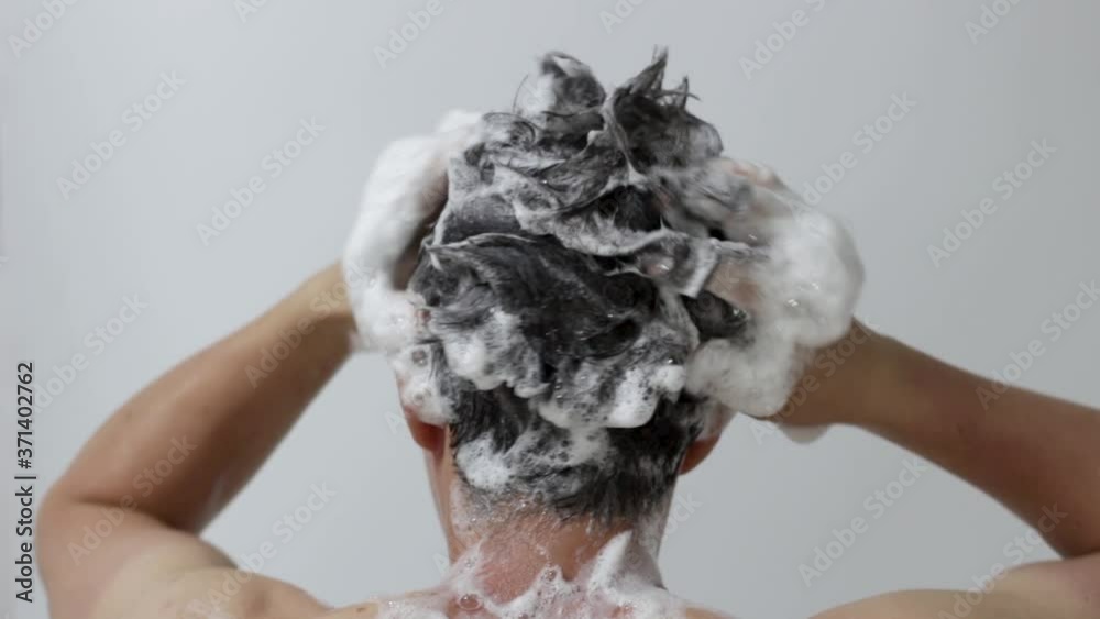 A man washes his head with shampoo on white background, rear view