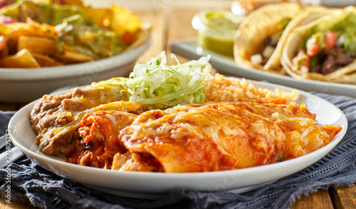 mexican enchilada platter with red sauce, refreied beans and rice photo