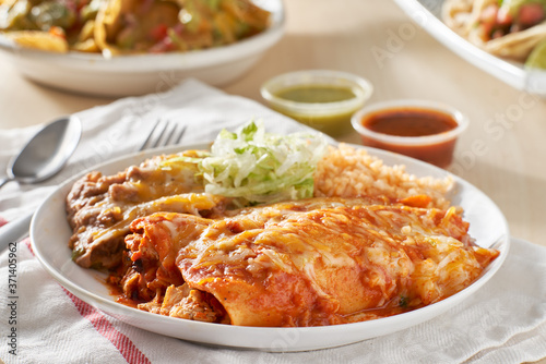 mexican enchilada platter with red sauce, refreied beans and rice photo