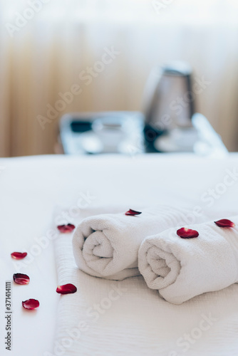Luxury hotel bedroom with white spa towels on bed sheet with rose petals and room service coffee. Romantic holiday weekend with wellness body treatment and relax couple massage in honeymoon suite.