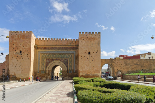 Meknes, Morocco - Okt.17,2018:Old city wall with Bab el-Khemis gate, entrance to the old city. People walking and old cars drive by. With a blue sky on a sunny day