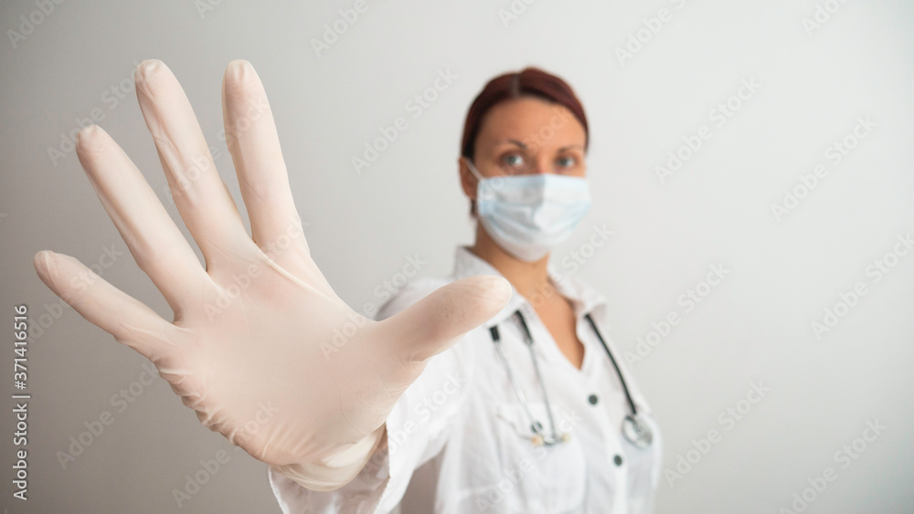 Woman with a white medical mask and latex glove shows the symbol STOP. Stopping the disease. Prevention of viruses. Negative space or copy space for text. Woman with a white medical mask and latex glove shows the symbol STOP. Stopping the disease. Prevention of viruses. Negative space or copy space for text.