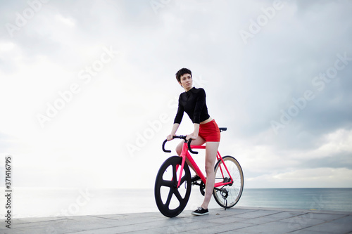 Stylish woman standing on the pier with her sport fixed gear bicycle enjoying the calm scenery against cloudy sky background with copy space area for your text message or content, female hipster rider photo