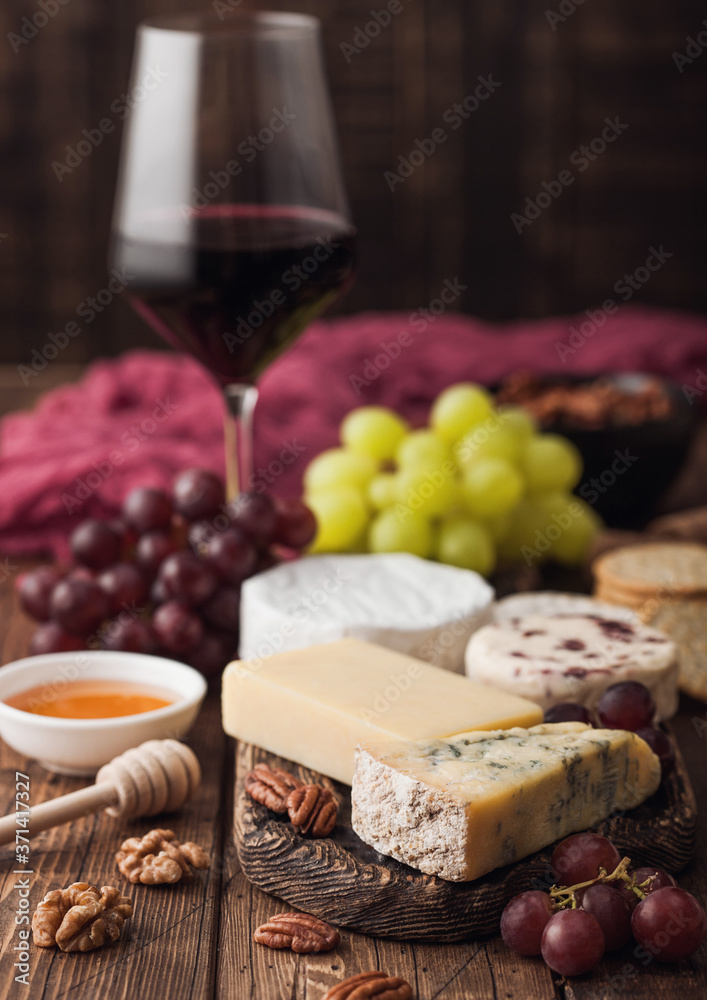 Glass of red wine with selection of various cheese and grapes on wooden background. Blue Stilton, Red Leicester and Brie Cheese and bowl of nuts and crackers. Top view Glass of red wine with selection of various cheese and grapes on wooden background. Blue Stilton, Red Leicester and Brie Cheese and bowl of nuts and crackers. Top view