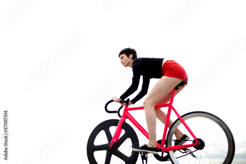 Fototapeta Naklejka Na Ścianę i Meble -  Portrait of young stylish woman cyclist enjoying fixed gear bike riding outdoors in a cloudy summer day while ride against the sky background with copy space area for your text message or content