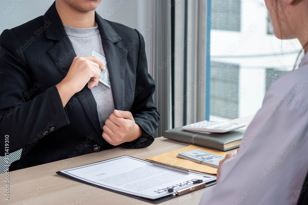 A businesswoman using a hand to pull money out of her suit pocket in order to bribe another employee, the anti-corruption concept. A businesswoman using a hand to pull money out of her suit pocket in order to bribe another employee, the anti-corruption concept.