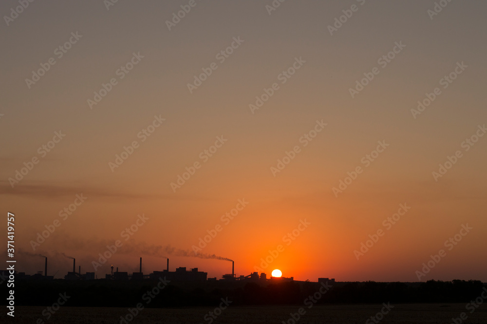 the setting sun on the background of smoking chimneys industry