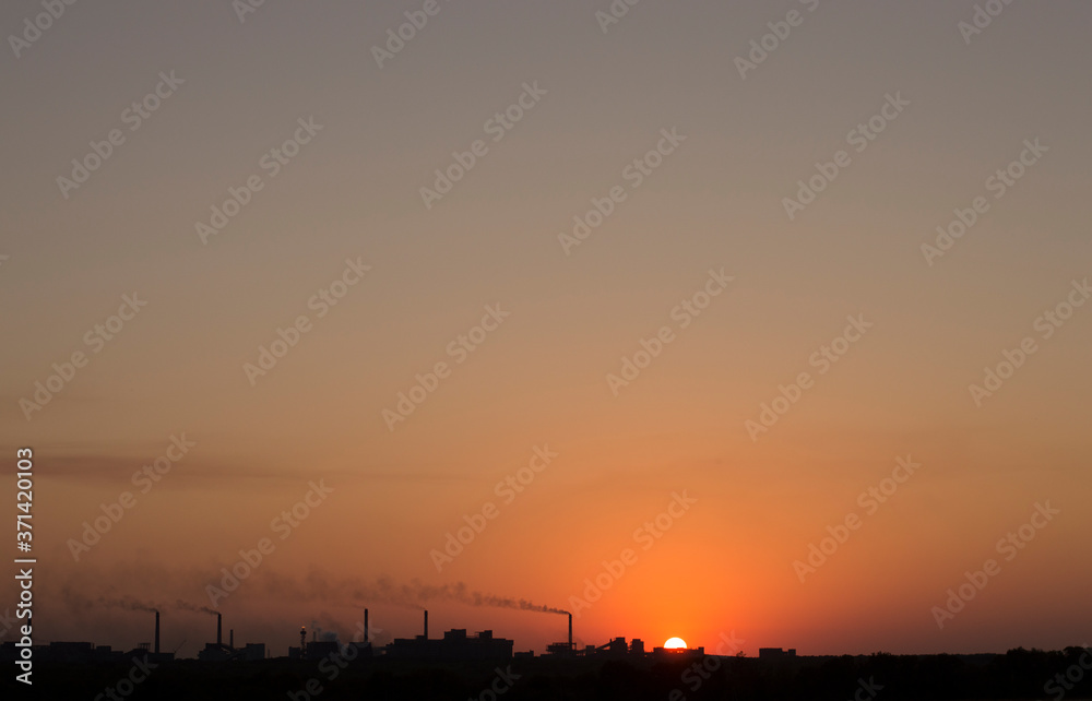 the setting sun on the background of smoking chimneys industry