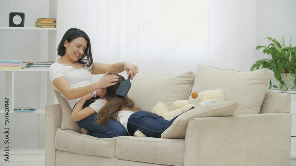 Littlle daughter is lying on mother's legs while mother is combing her hair, talking with her, and petting her head. Littlle daughter is lying on mother's legs while mother is combing her hair, talking with her, and petting her head.