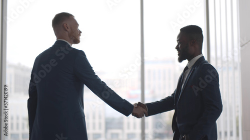Two confident diverse businessmen shaking hands during meeting in office