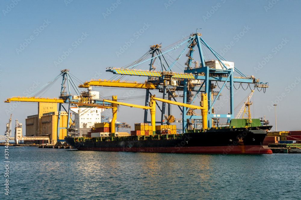 Port Sudan, Sudan. Large container ship being loaded with containers and cargo in port in Port Sudan. Huge port cranes loading cargo.