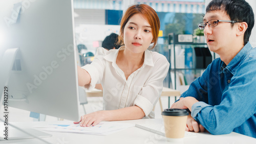 Millennial group of young Asia businessman and businesswoman in small modern urban office. Japanese male boss supervisor teaching intern or new employee korean girl helping with difficult assignment.