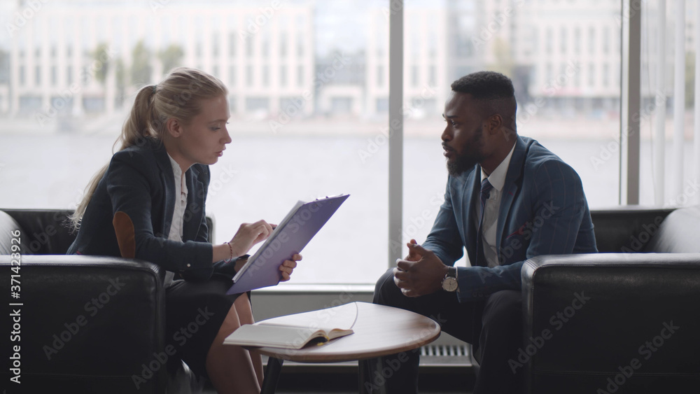 Young HR woman interviews afro-american male candidate for job sitting on couch in conference room Young HR woman interviews afro-american male candidate for job sitting on couch in conference room