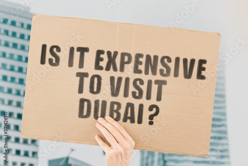Canvas Print The question  Is it expensive to visit Dubai?  on a banner in men's hand with blurred background