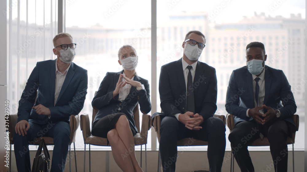 Business people wearing safety masks sitting on chairs in office corridor and waiting in queue Business people wearing safety masks sitting on chairs in office corridor and waiting in queue