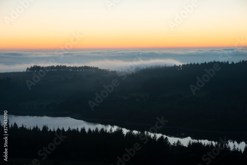 Majestic landscape image of cloud inversion at sunset over Dartmoor National Park in Engand with cloud rolling through forest on horizon