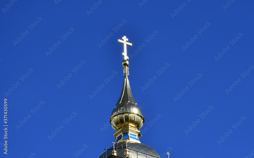 The dome of the Orthodox Church with a Golden cross against the blue sky.