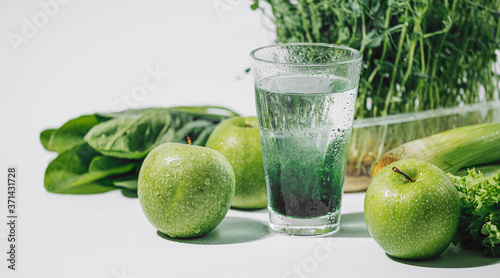 chlorophyll in a glass of water on a white background near are various fresh vegetables fruits and roots with lettuce and spinach photo