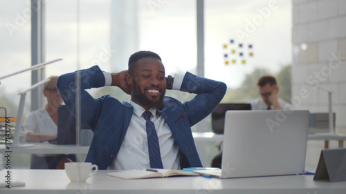 Happy afro businessman with hands behind head smiling resting at desk in office.