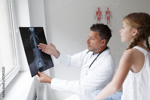 Doctor in white coat examines girl's back and shows X-ray in hospital