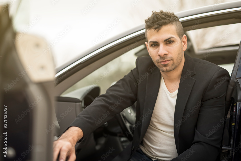 Young man posing in suit near t his luxury car