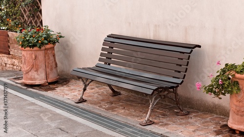 Isolated black bench in the courtyard near two vases with plants and flowers in front of the wall  Italy  Europe 