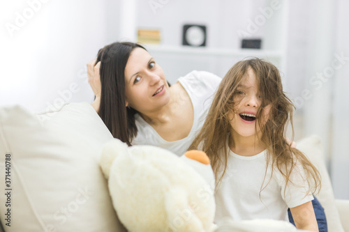 Photo of beautiful mom and her little daughter smiling while sitting on couch at home.